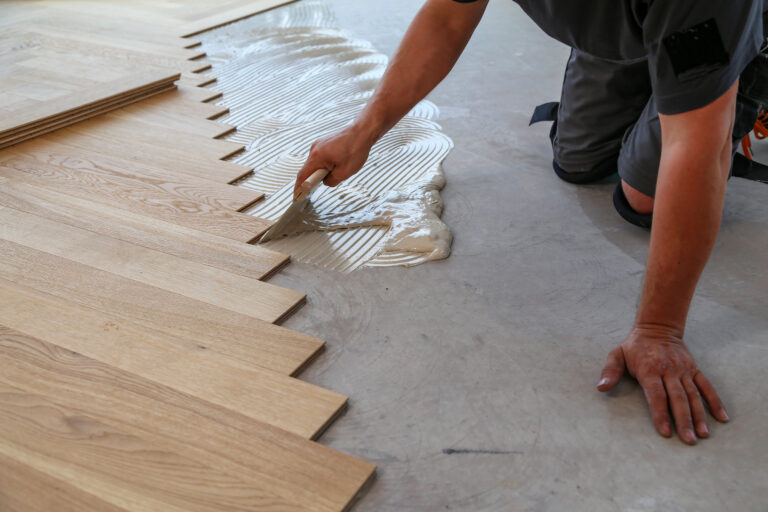 A male worker installing a wooden laminate flooring on his knees